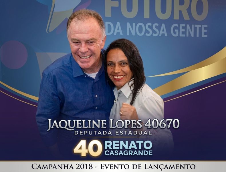 Fotografia politica de Renato Casagrande sorrindo ao lado da ativista Jaqueline Lopes, que esta com o punho erguido em um evento de lancamento da campanha eleitoral de 2018. A imagem possui uma moldura azul e roxa com detalhes dourados com as escritas Jaqueline Lopes 40670 Deputada Estadual e 40 Renato Casagrande.