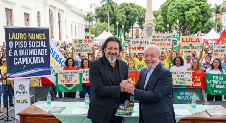 Revista Raio-X | SERRA-ES: O Salário Mínimo como Piso da Dignidade: A Batalha pela Emancipação Social e Valorização da Renda no Brasil O pré-candidato a deputado estadual Lauro Nunes (PV-ES) aperta a mão do presidente Lula em ato público com bandeiras da Federação Brasil da Esperança e faixas sobre o salário mínimo regional e combate à miséria no Espírito Santo.